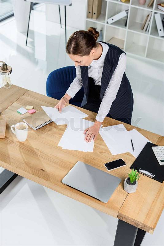 Young businesswoman in office, standing over her desk and examining paperwork, stock photo