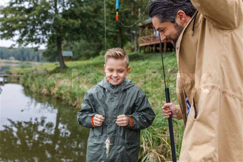 Father and son caught a little fish with fishing rod on lake, stock photo