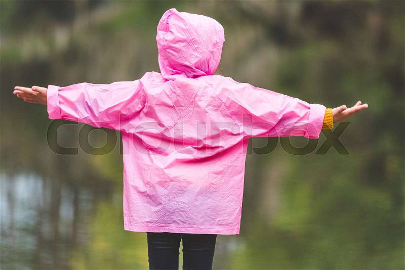 Rear view of kid in pink raincoat with outstretched arms, stock photo
