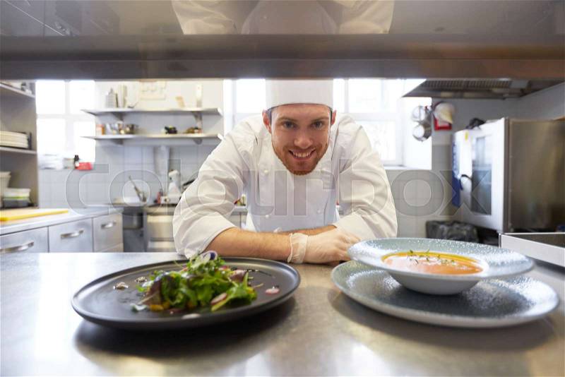 Food cooking, profession and people concept - happy male chef cook with plate of soup and salad at restaurant kitchen table, stock photo