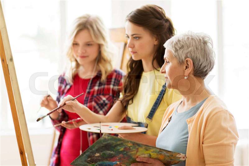 Art school, creativity and people concept - women artists with easel, paint brushes and palettes painting at studio, stock photo