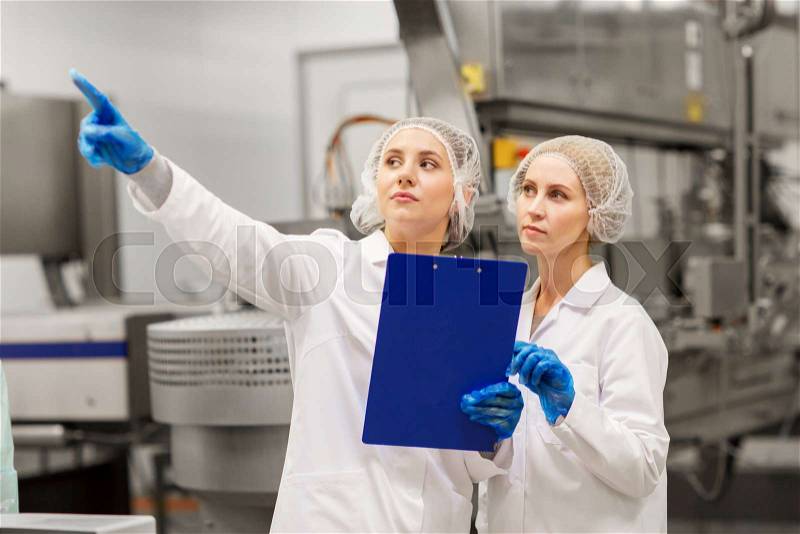 Manufacture, industry and people concept - women technologists with clipboard at ice cream factory shop, stock photo