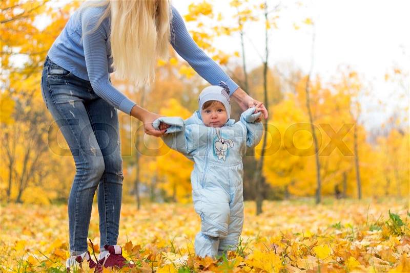 First steps of little kid in autumn park. Mother teaching her cute little son to walk, stock photo