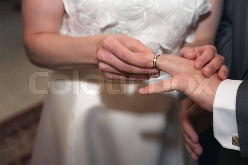 Hands of the groom and bride is wearing a ring on the finger on the day of the wedding ceremony. Gold, symbol, religion, love, stock photo