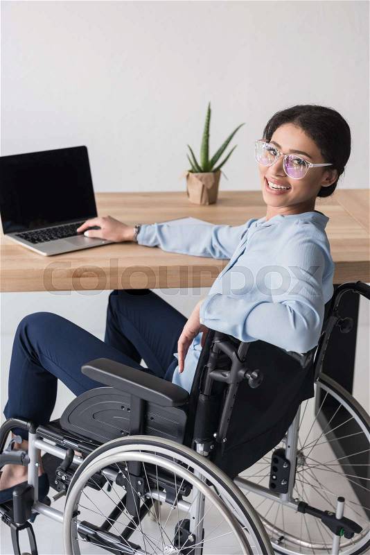 Smiling disabled african american businesswoman working on laptop at workplace, stock photo
