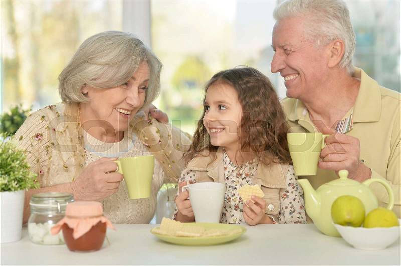 Grandparents with granddaughter drinking tea at home, stock photo
