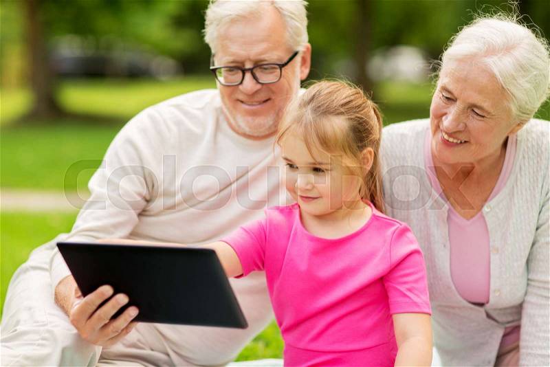 Family, generation and technology concept - happy smiling grandmother, grandfather and little granddaughter with tablet pc computer sitting on blanket at park, stock photo