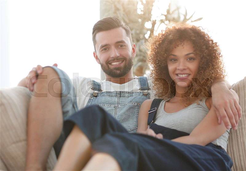 Young couple in work clothes sitting on couch in new house, stock photo