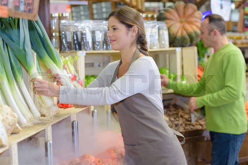 Smiling beautiful female seller posing with leeks in supermarket, stock photo