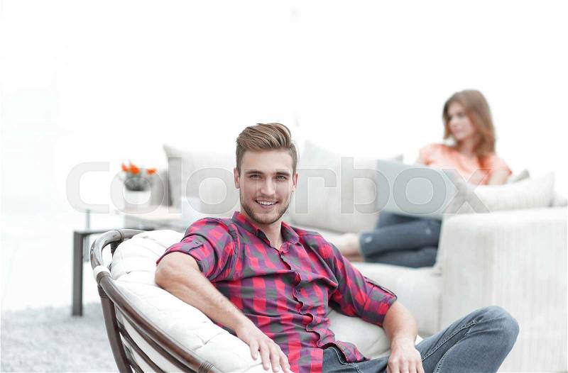 Smiling young male sitting in a big chair on blurred background, stock photo