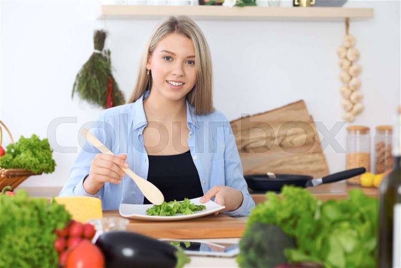 Girl following recipe on digital tablet while cooking in kitchen. Healthy meal and culinary concept, stock photo