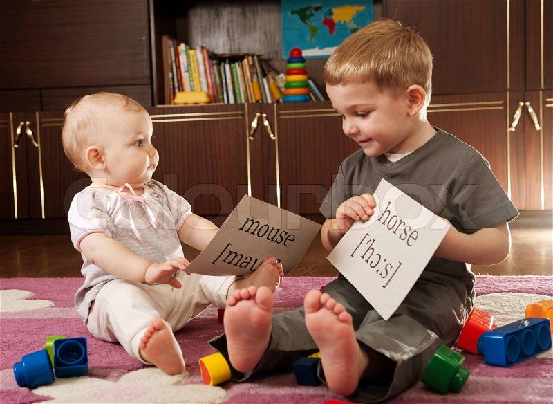 A boy aged three and a girl aged one are playing with blocks and cards with words, stock photo