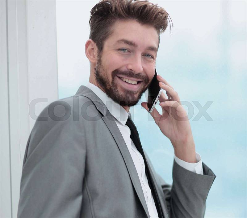 Handsome smiling business man in an office using smartphone, stock photo