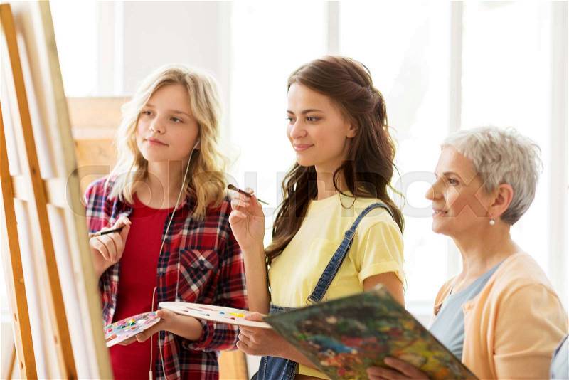 Art school, creativity and people concept - women artists with easel, paint brushes and palettes painting at studio, stock photo