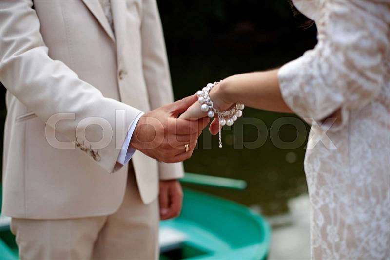The groom gently holds the bride by the hand, close-up, stock photo