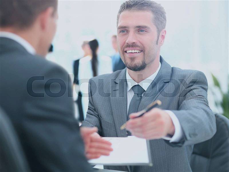 Businessman giving a pen to seal deal with his partner, stock photo