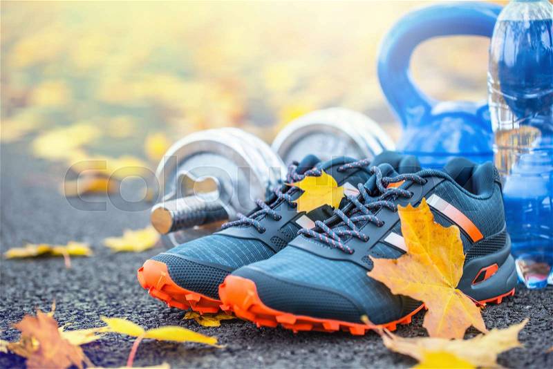 Pair of blue sport shoes water and dumbbells laid on a path in a tree autumn alley with maple leaves - accessories for run exercise or workout activity, stock photo