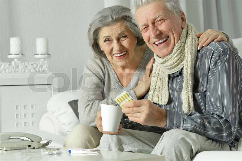 Ill senior couple sitting at table and taking pills, stock photo