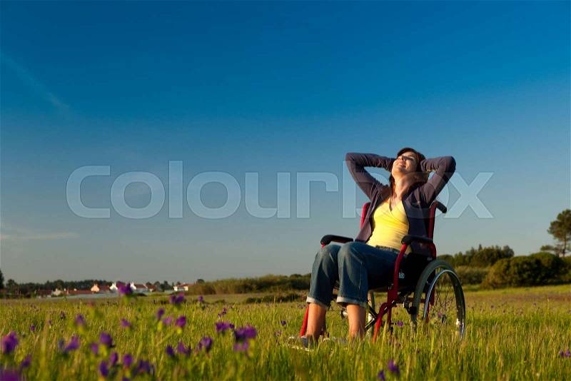 Handicapped woman on a wheelchair over a green meadow, stock photo