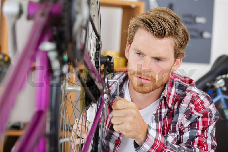 Young man fixing bike wheel in store, stock photo