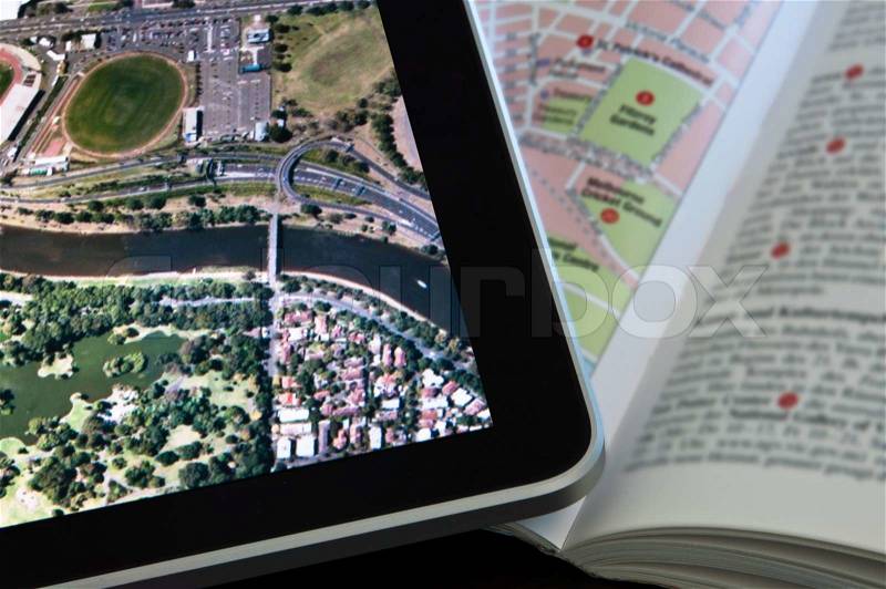 Modern Tablet PC displaying a city map with classic printed travel guide next to it, stock photo