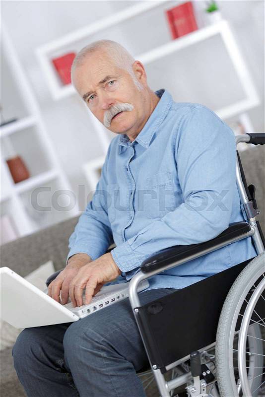 Mature man in a wheelchair working on a laptop, stock photo