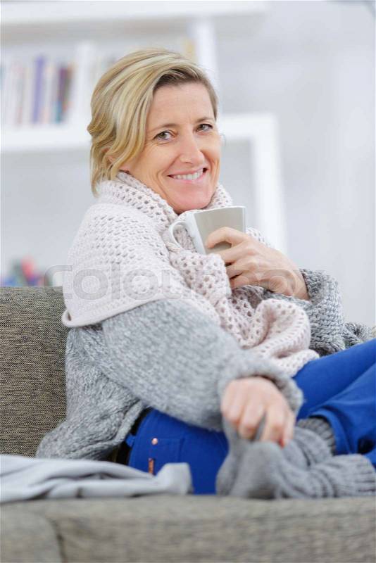 Beautiful ill woman sitting on couch at home and smiling, stock photo