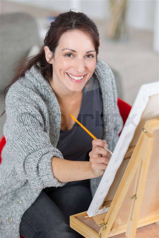Mature bautiful woman painting on a canvas at home, stock photo
