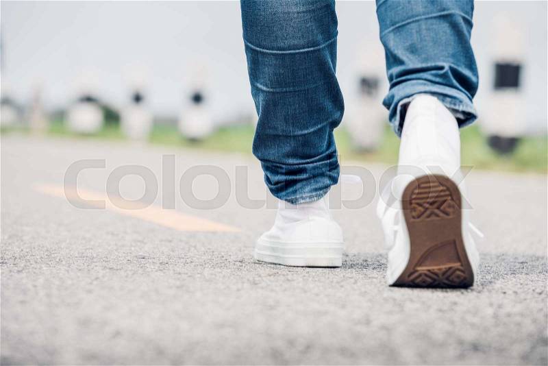 Close up woman wear jean and white sneaker walking forward on highway road in sunny day,Alone travel or solo traveler concept, stock photo