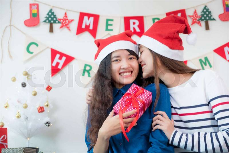 Asia lover Girlfriend kiss cheek and give Christmas gift at xmas party,Asia girl friends wear santa hat exchange red gift box with smiling face,gift giving,Lovely lesbian couple, stock photo