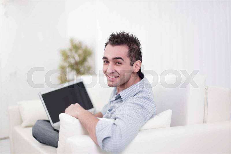 Handsome man is using a laptop, looking at camera and smiling, stock photo