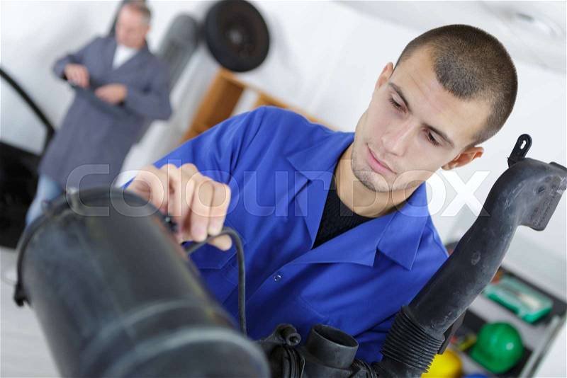 Apprentice mechanic working on exhaust pipe in auto repair shop, stock photo