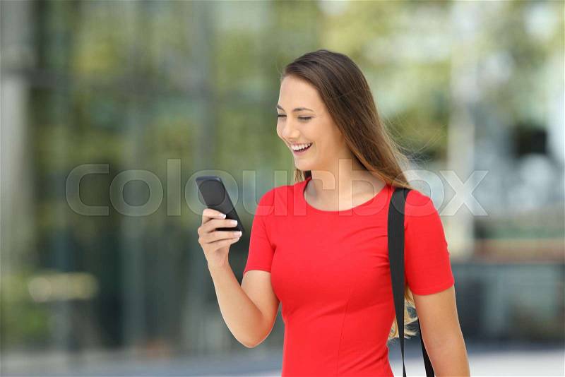 Single entrepreneur wearing a red dress reading on line content in a mobile phone walking on the street, stock photo