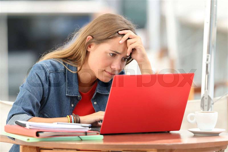 Single worried student searching on line content in a laptop sitting in a coffee shop outdoors, stock photo