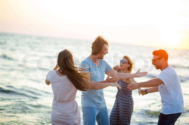Group of cheerful young people dances having joined hands on the beach. Summer, waves, sea wind, sunset. Friends a lot of fun, stock photo