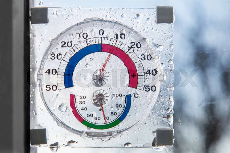 Hygrometer, thermometer all in one behind window in rainy weather, stock photo