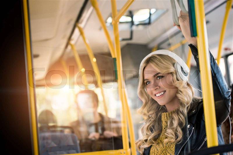 Beautiful happy young woman in headphones listening music in bus, stock photo