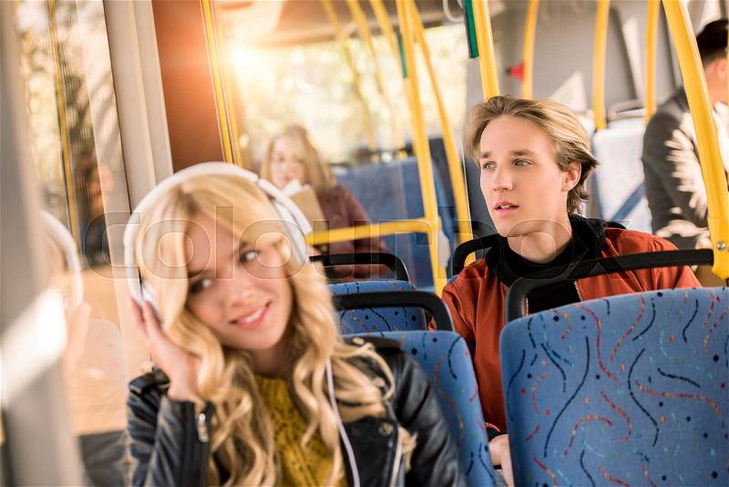Young man looking at window and smiling girl listening music in city bus, stock photo