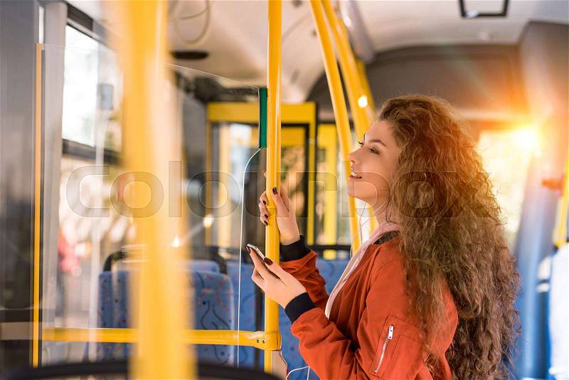 Beautiful smiling young woman using smartphone in city bus, stock photo