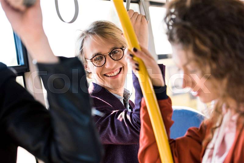 Selective focus of happy young man in eyeglasses smiling at camera in bus, stock photo