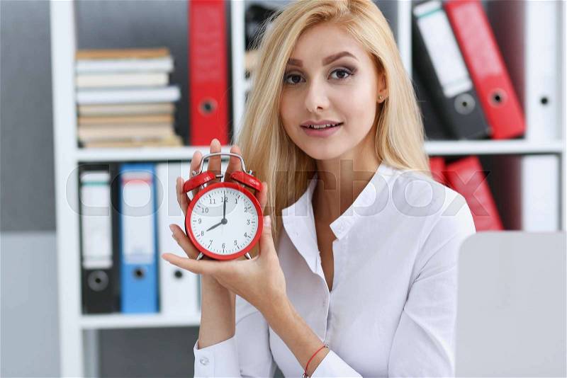 Smiling business woman holding in hand on the alarm clock a red color showing eight o\'clock in the morning or evening AM PM, stock photo