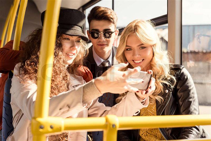 Portrait of smiling friends taking selfie in public transport, stock photo