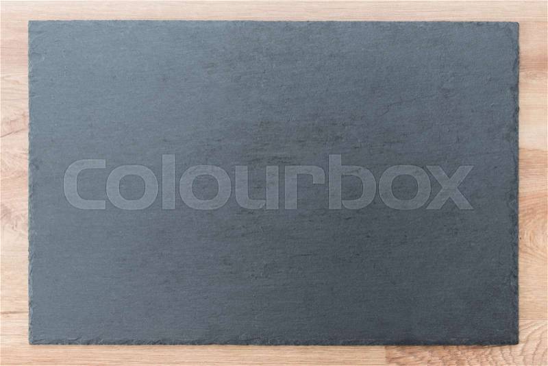 Slate board on wooden background. Black and gray slate textured flat stone laying on brown wooden desk table background, top view, copy space for text or menu concept, stock photo