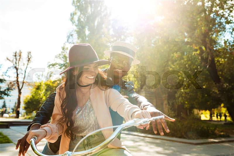 Lovely multicultural couple riding one bike together in a sunny day , stock photo