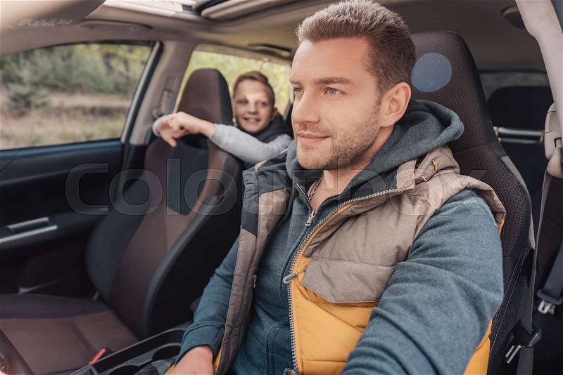 Smiling little son looking at father driving car, stock photo