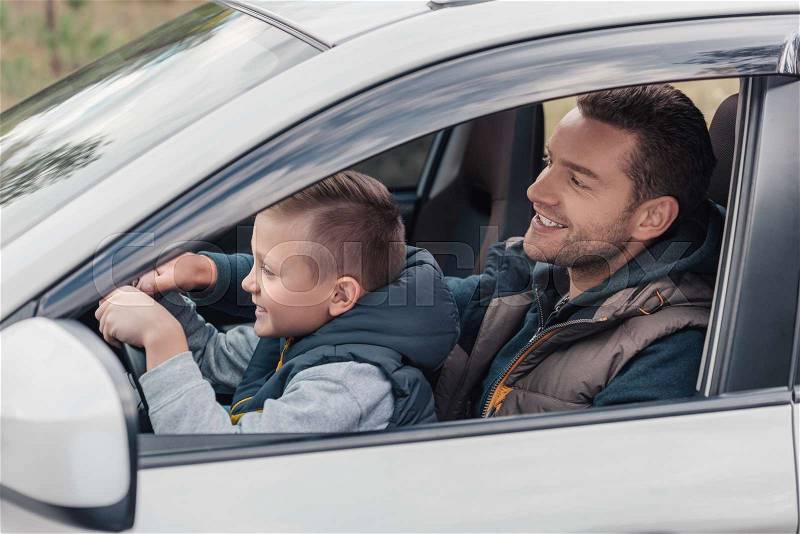 Side view of happy father and son driving car together, stock photo
