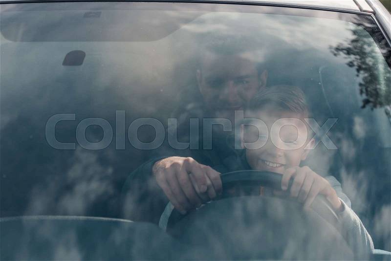 View through window of father and son driving car together, stock photo