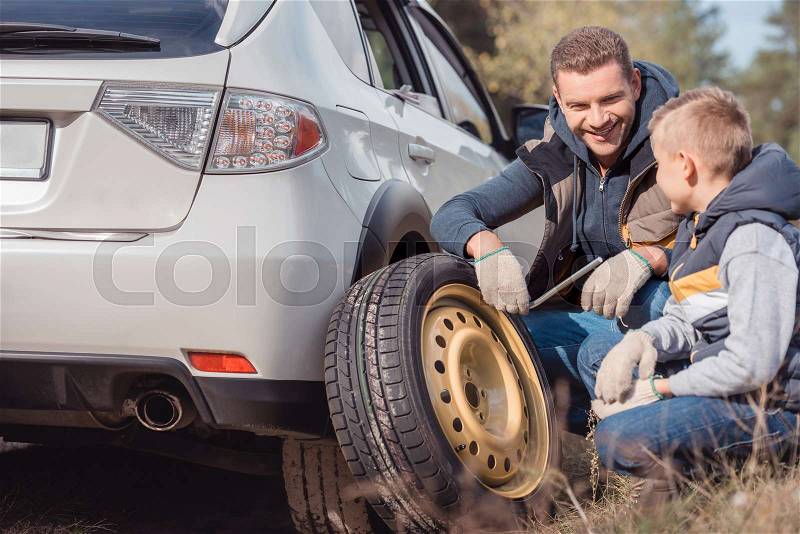 Smiling father and son changing car wheel together, stock photo