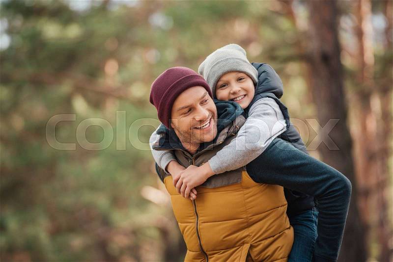 Happy father piggybacking adorable smiling son in forest, stock photo