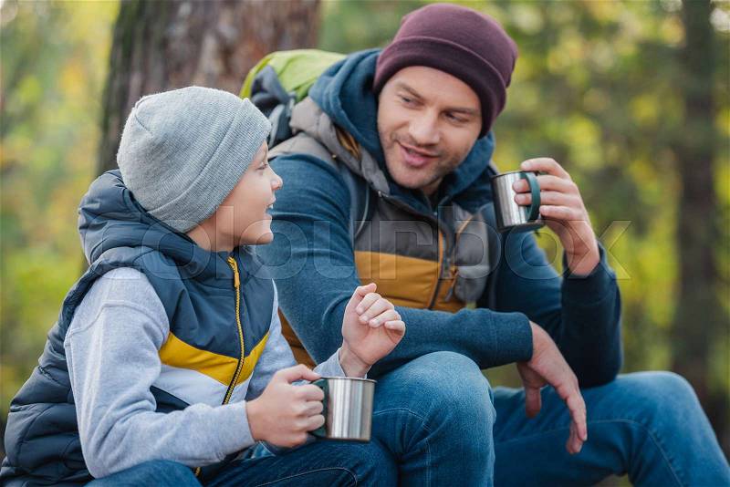 Smiling father and son drinking tea from thermos in autumn forest, stock photo